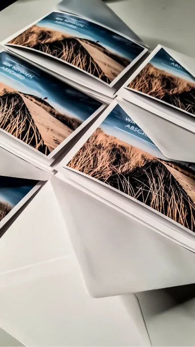 Faltkarten mit Landschaftsaufnahmen einer Dünenlandschaft auf einem Tisch.