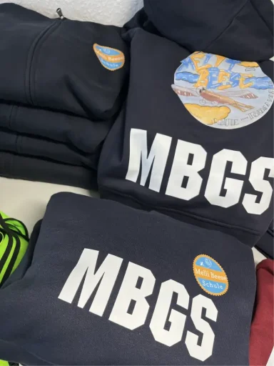 Dunkelblaue Sweatshirts mit dem Aufdruck "MBGS" und buntem Markenlogo.