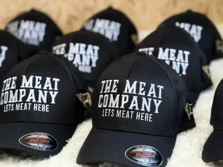 Schwarze Kappen mit dem Schriftzug "The Meat Company" in weißer Schrift.