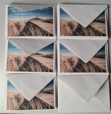 Sechs weiße Umschläge mit Landschaftsdruck einer sandigen Küste und blauen Himmel.