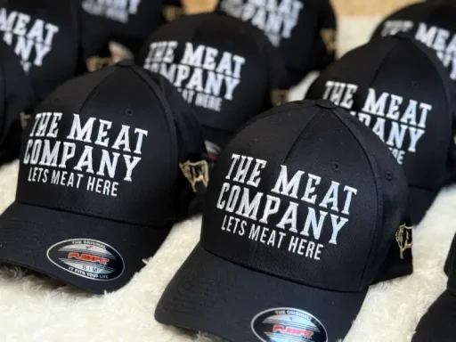 Schwarze Baseballmützen mit dem Schriftzug "The Meat Company" in Weiß.