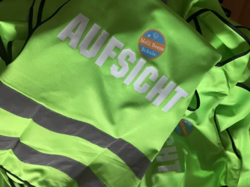 Grüne Sicherheitswesten mit dem Aufdruck „AUFSICHT“ und reflektierenden Streifen.