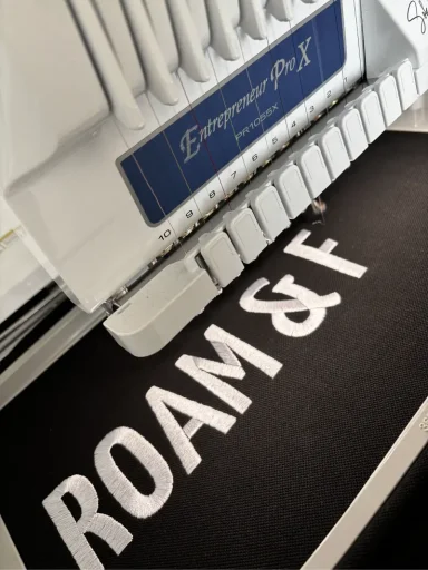 Stickmaschine mit dem Schriftzug "ROAM & F" auf schwarzem Stoff.