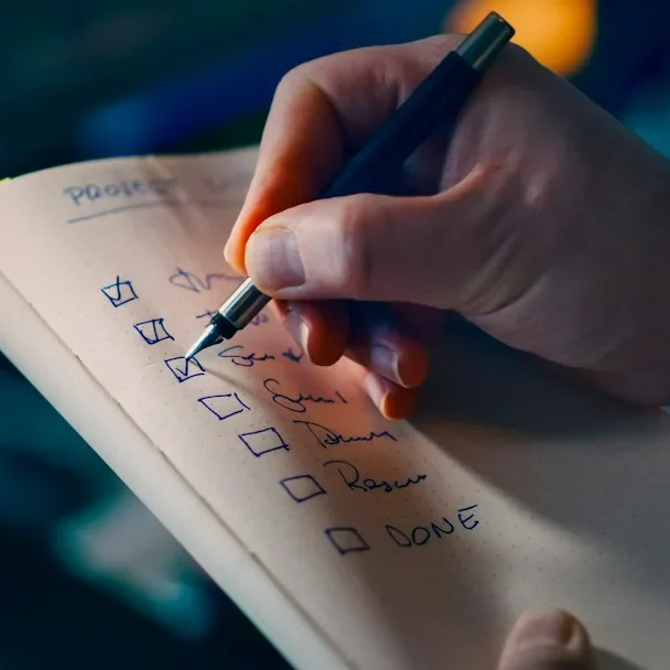 Hand hakt einzelne Schritte auf einer Checkliste im Notizbuch ab.