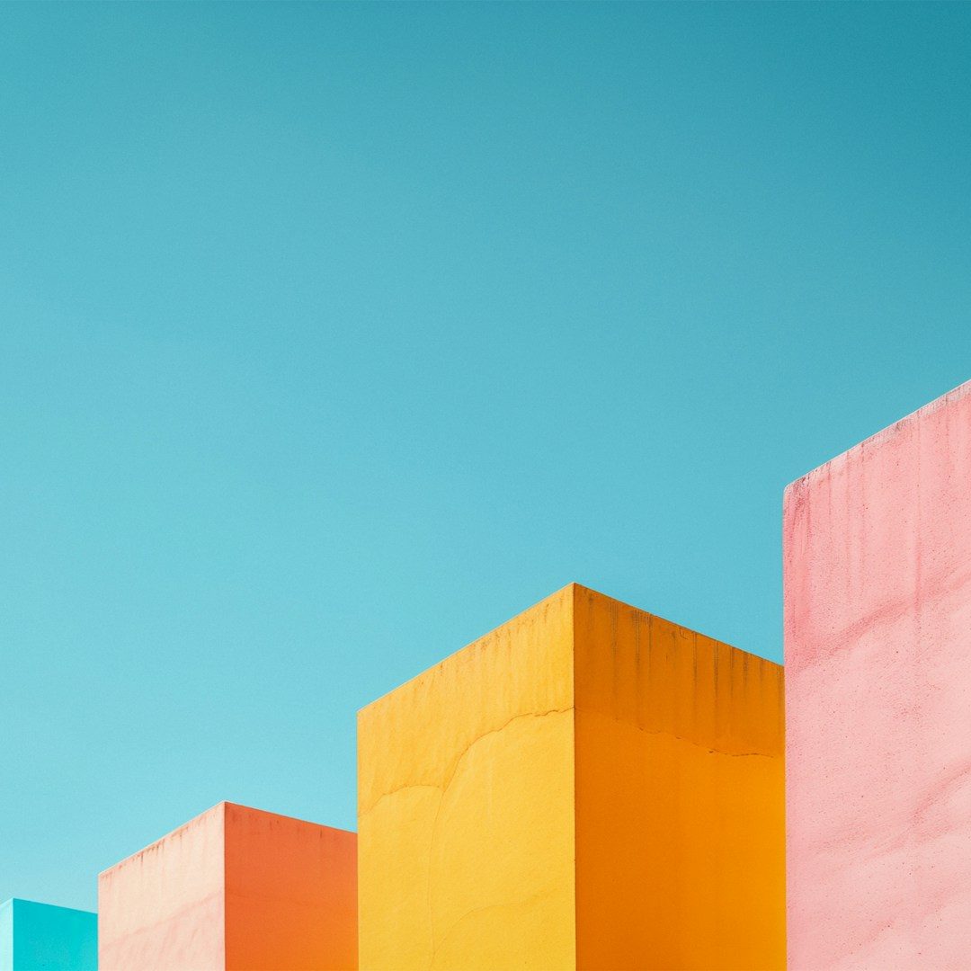 Bunte geometrische Formen in Gelb, Pink, Blau und Orange vor einem klaren Himmel.