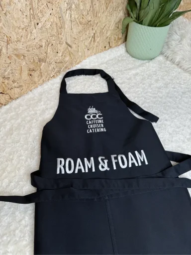 Schwarze Schürze mit dem Schriftzug "ROAM & FOAM" darauf.