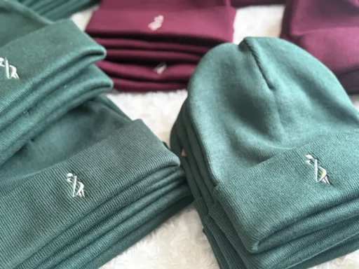 Grüne und burgunderfarbene Mützen liegen gestapelt auf einem hellen Hintergrund.