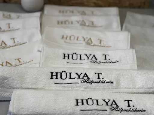 Mehrere weiße Handtücher mit der Aufschrift "HÜLYA T." in verschiedenen Farben.