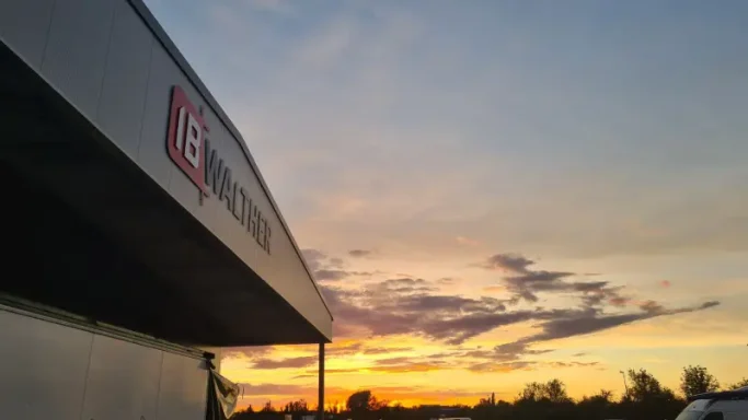 Fassadenschild Sonnenuntergang mit wolkenverhangenen Himmel hinter einem Gebäude.