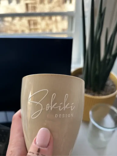 Beige Tasse mit dem Namen "Bohiki" und Pflanze im Hintergrund.