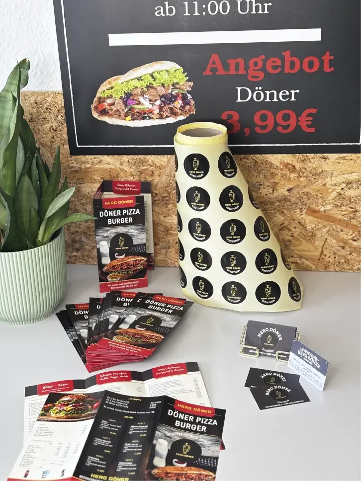 Blick auf ein Tischarrangement mit Speisekarten, Prospekten und einem Topf mit Pflanze.