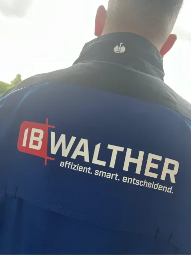 Person trägt eine blaue Jacke mit dem Logo "IB WALTHER" auf dem Rücken.