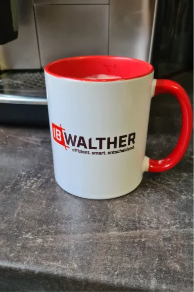 Weißer Kaffeebecher mit rotem Henkel und Aufschrift "WALTHER".
