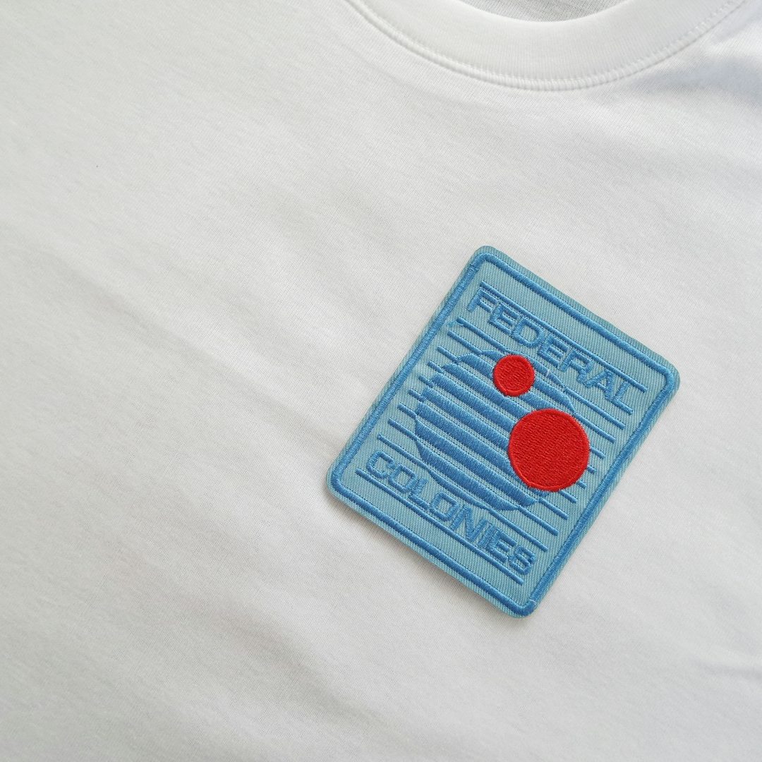 Gesticktes Patch auf weißem T-Shirt mit blauen Linien und roten Kreisen.