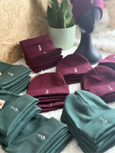 Eine Auswahl an roten und grünen Mützen auf einem Tisch, ergänzt durch eine Pflanze.