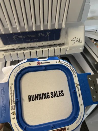 Stickrahmen mit der Aufschrift "RUNNING SALES" auf einem Stickgerät.