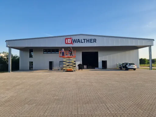 Schild Montage Helles Lagergebäude mit geöffnetem Tor und abgestellt Fahrzeug auf dem Parkplatz.