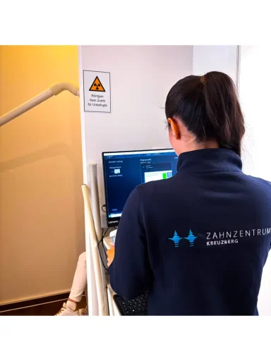 Person in dunklem Pullover arbeitet an einem Computer vor einer Wand mit Warnschild.