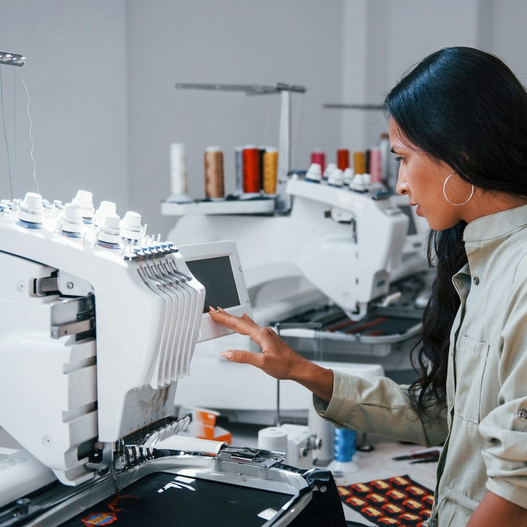 Person arbeitet konzentriert an einer modernen Stickmaschine in einem hellen Raum.