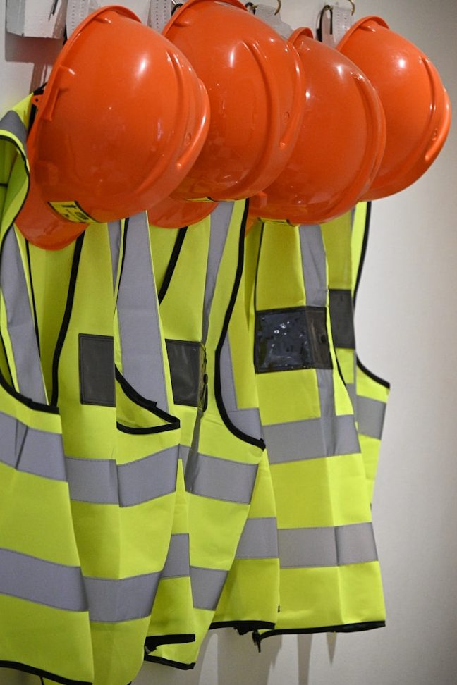 Orange Helme und leuchtend gelbe Sicherheitswesten hängen an mehreren Haken.
