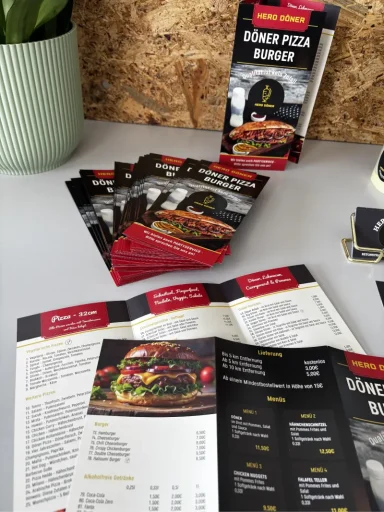 Menü und Werbematerialien für ein Restaurant auf einem Tisch, mit einer Pflanze im Hintergrund.