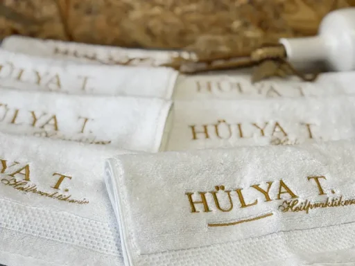 Weiße Handtücher mit goldener Schrift "HÜLYA T." auf strukturierter Oberfläche.
