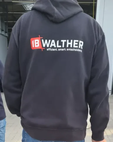 Schwarze Jacke mit dem Logo "IB WALTHER" auf dem Rücken.