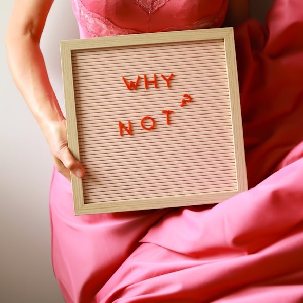 Eine Person hält ein Schild mit der Aufschrift "WHY NOT?" in leuchtendem Orange.