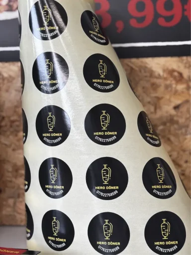 Braunes Papier mit schwarzen, runden Aufklebern und goldenem Logo. Preis: 3,99 €.