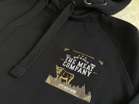 Schwarzer Hoodie mit dem Logo der "The Meat Company" in goldener Schrift.