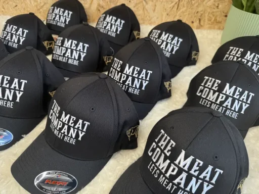 Schwarze Caps mit dem Aufdruck "THE MEAT COMPANY" in weißen Buchstaben.