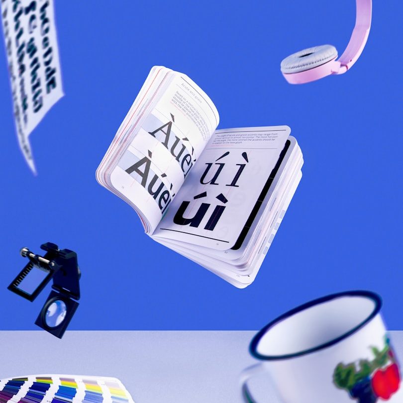 Ein offenes Buch mit Text, Kamera, Farbpalette, Tasse und Tape vor blauem Hintergrund.