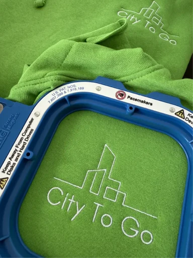 Grüne Sweatshirts mit gesticktem Logo "City To Go" in einem Stickrahmen.