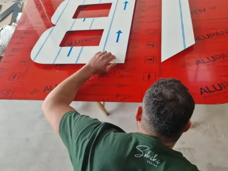 Eine Person arbeitet an roten Schildern mit blauen Markierungen für eine Beschriftung.