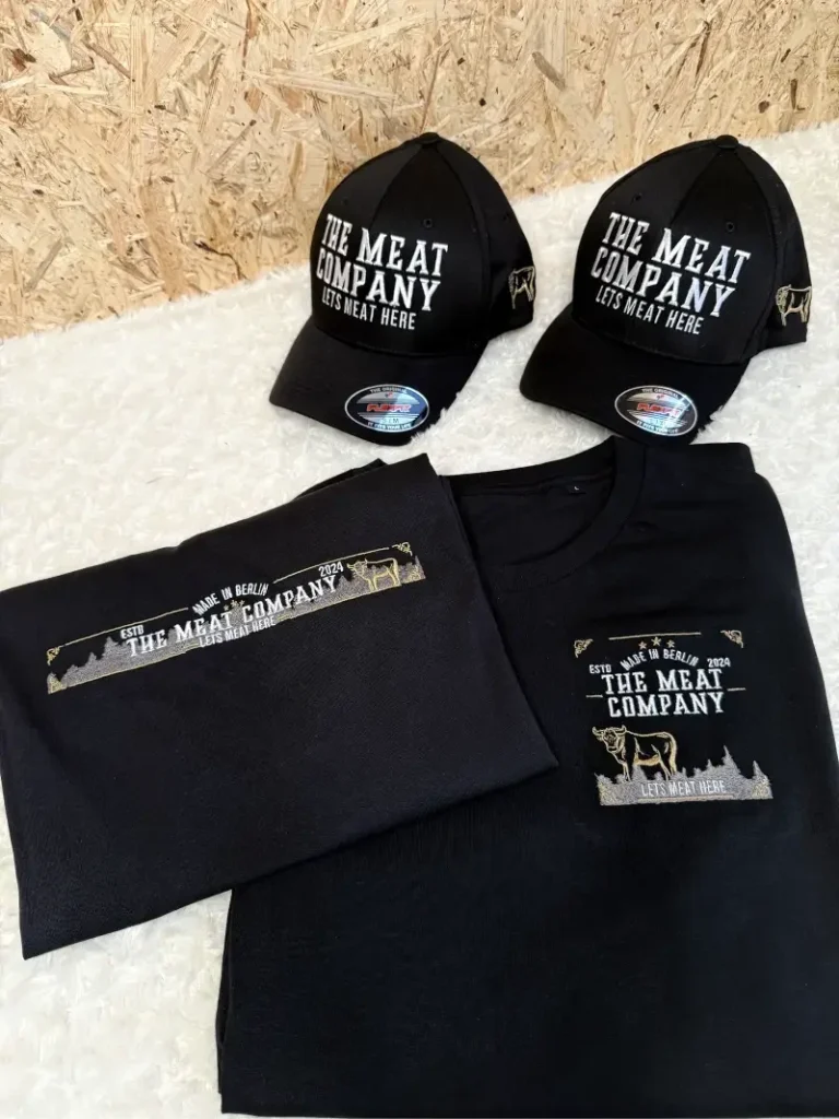 Schwarzes T-Shirt und zwei schwarze Caps mit Schriftzügen in Weiß.