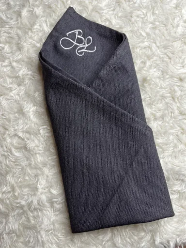 Dunkelgrau gefaltete Serviette mit eingeziertem monogrammierten Buchstaben.