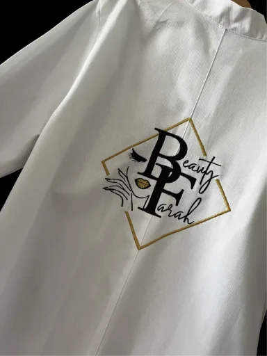 Weißer Kittel mit schwarzem und goldenem "Beauty Pearl"-Logo.